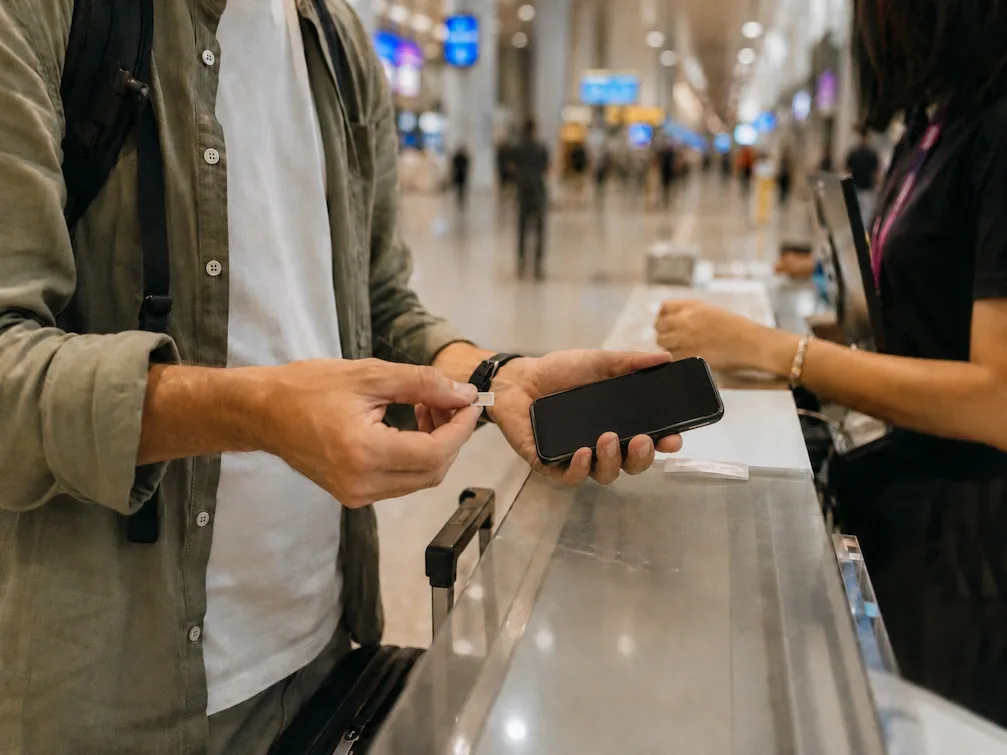 A traveler at an airport counter handing their phone across to set up a local SIM