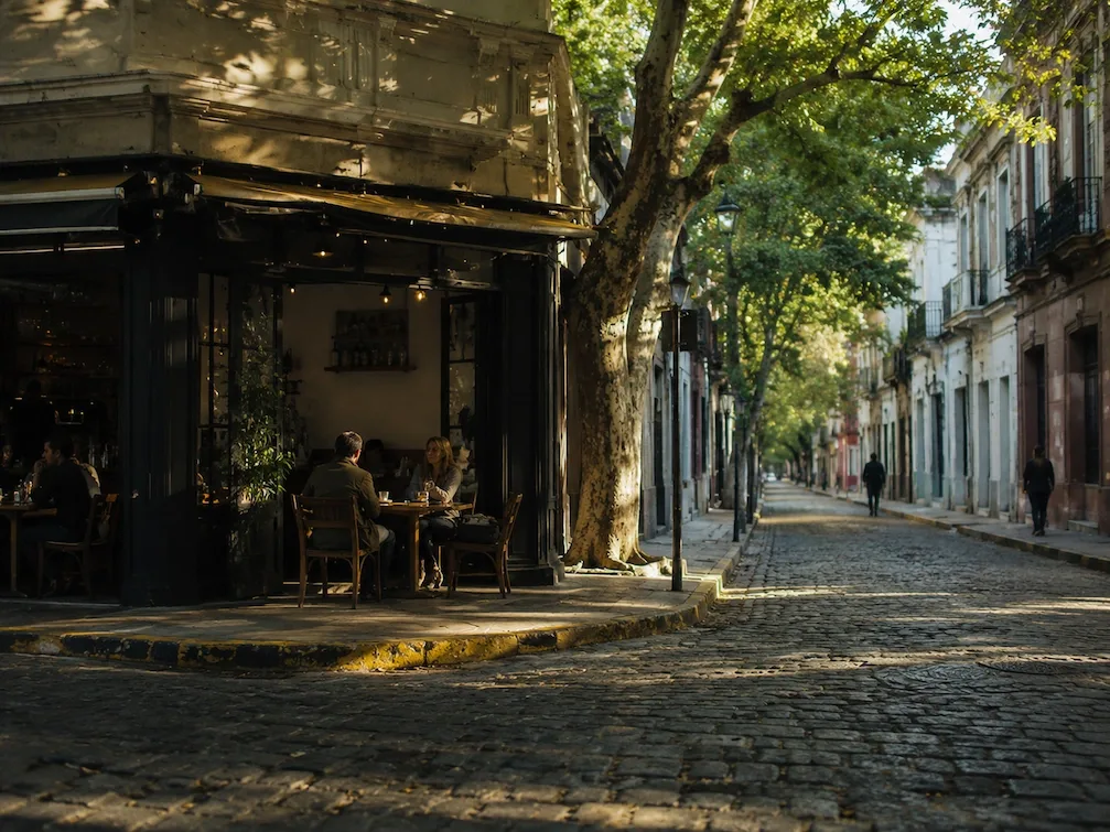 A quiet cobblestoned San Telmo street at dusk, cafe tables under the trees