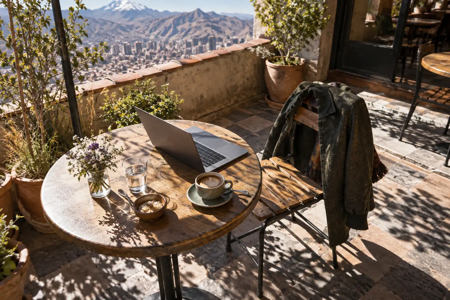 A Sopocachi café patio under hard dry-season sun, a laptop and a jacket on the chair