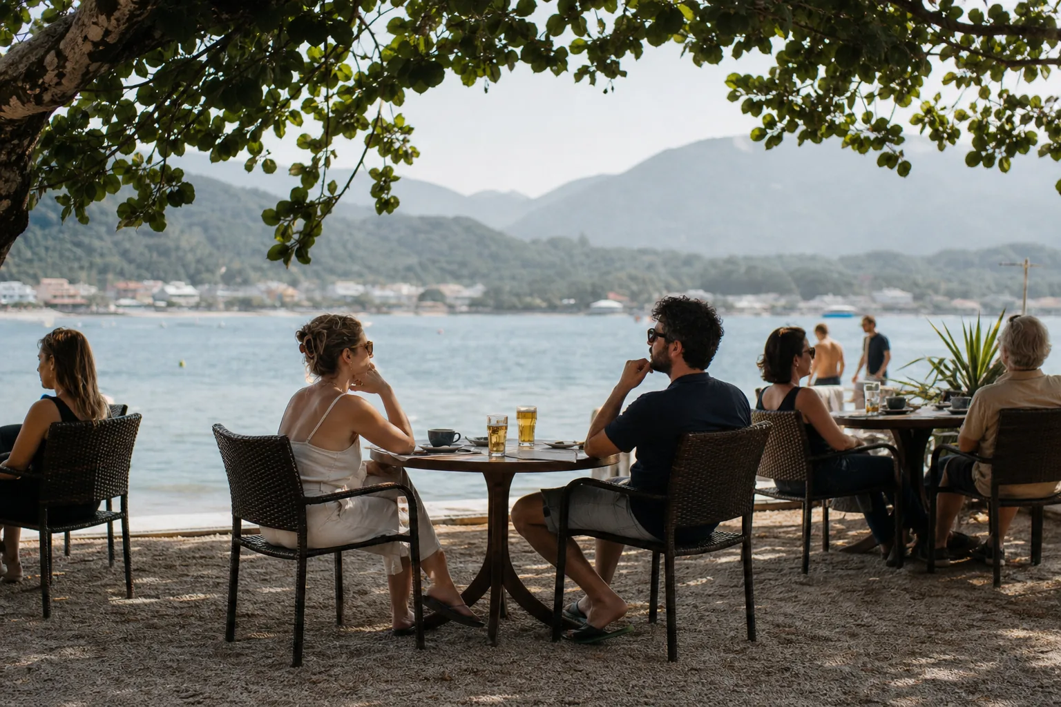 Cafe tables along the lakefront in Lagoa da Conceicao, Florianopolis, with hills and a hazy sky beyond the water
