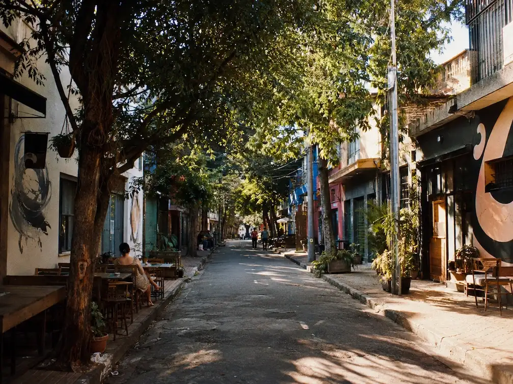 A leafy, low-rise Vila Madalena street by day, cafe tables and a hint of street art