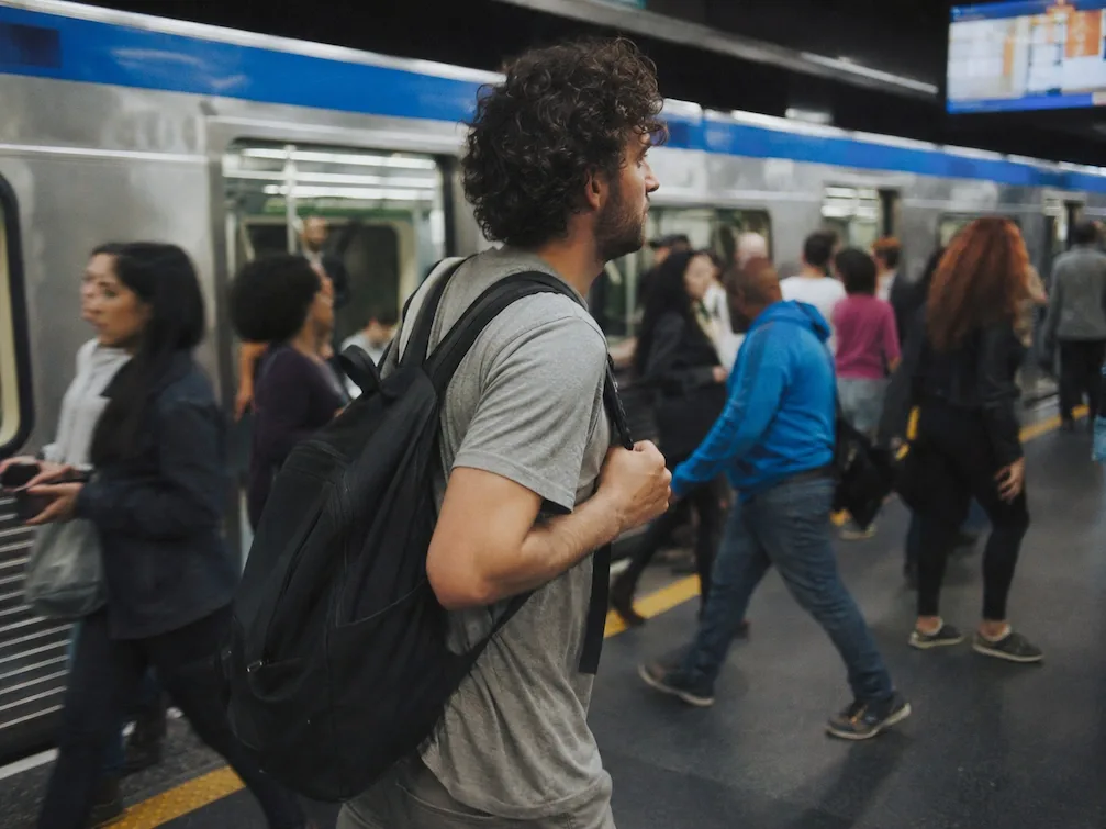 A traveler with a backpack on a busy São Paulo Metrô platform as commuters move past a blue-striped train