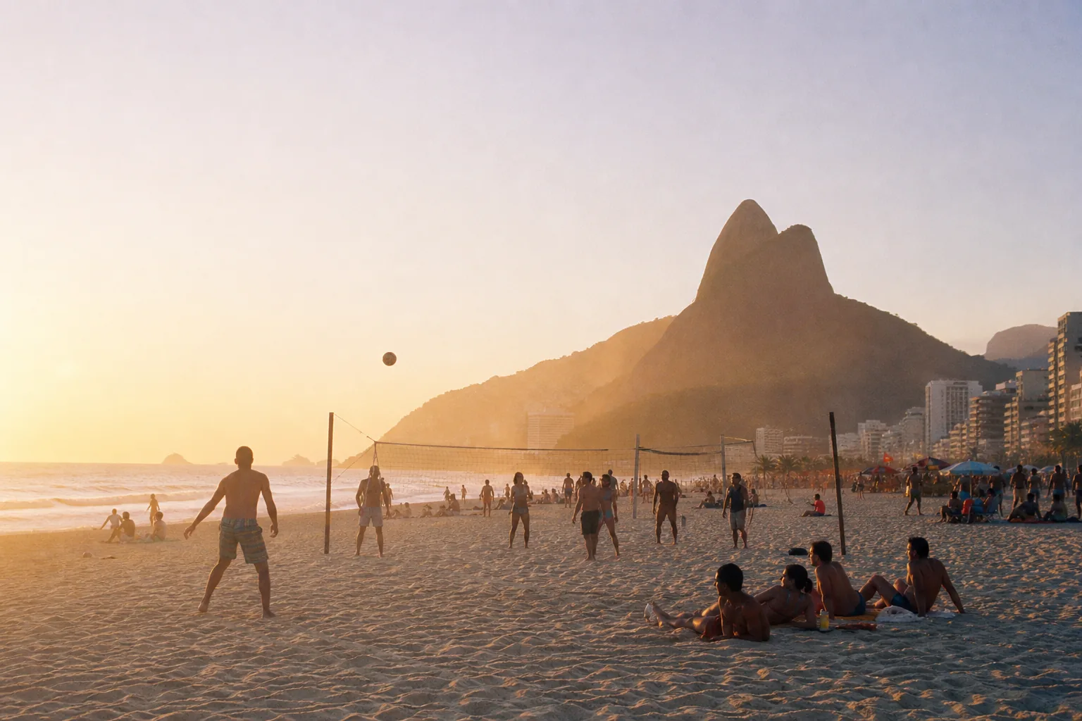 A crowded Ipanema beach at golden hour with Dois Irmãos mountain rising behind the sand
