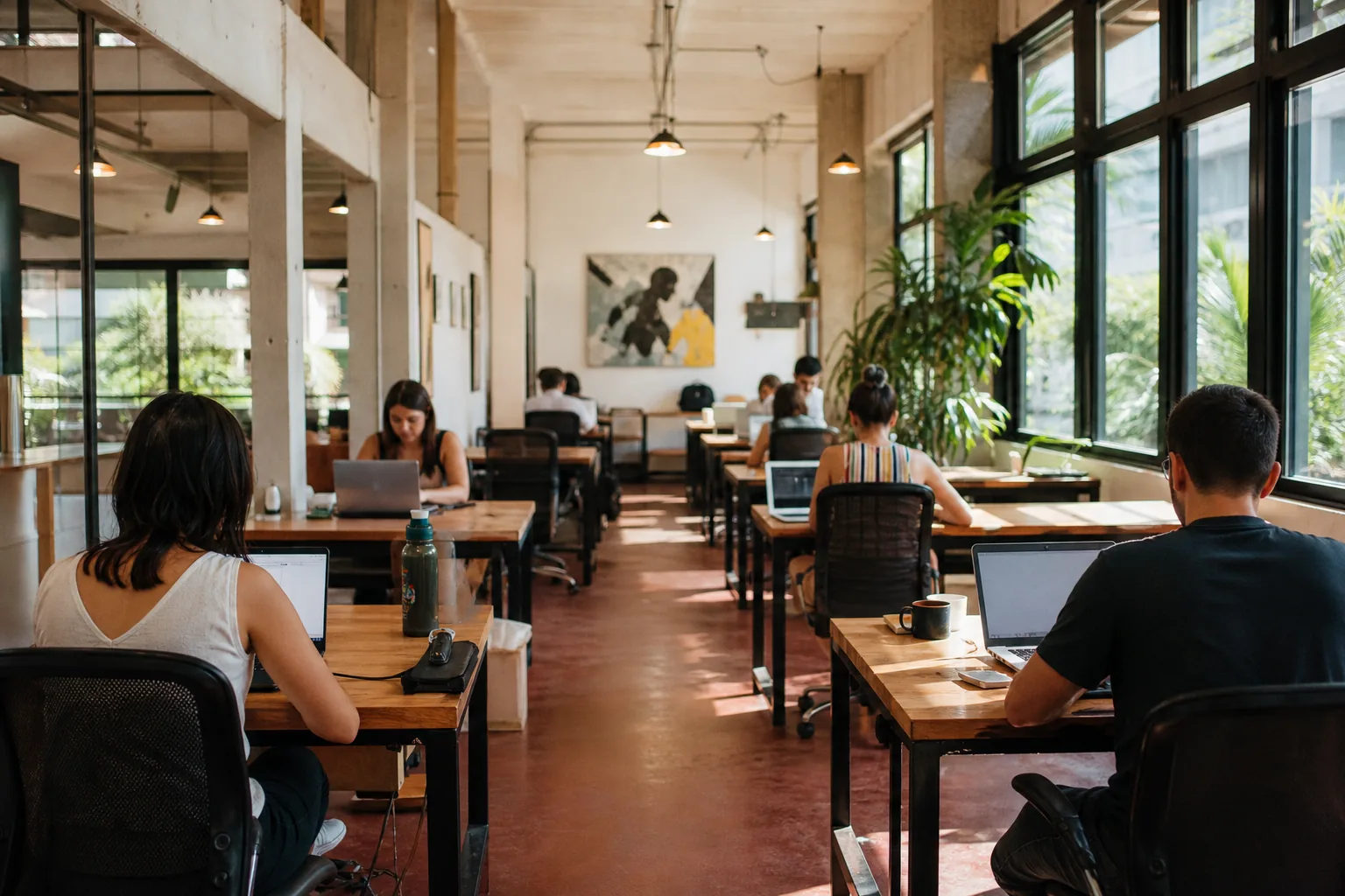 Rows of desks inside a bright coworking space in Centro, Florianopolis, with large windows and people working on laptops