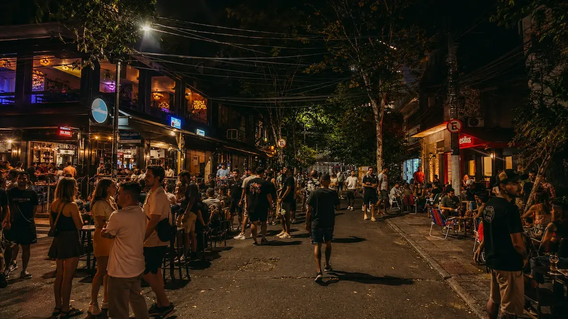 A packed outdoor bar street in Vila Madalena, São Paulo, glowing under string lights at night.