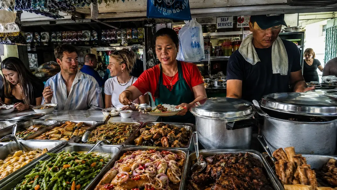 A carinderia counter lined with trays of Filipino dishes