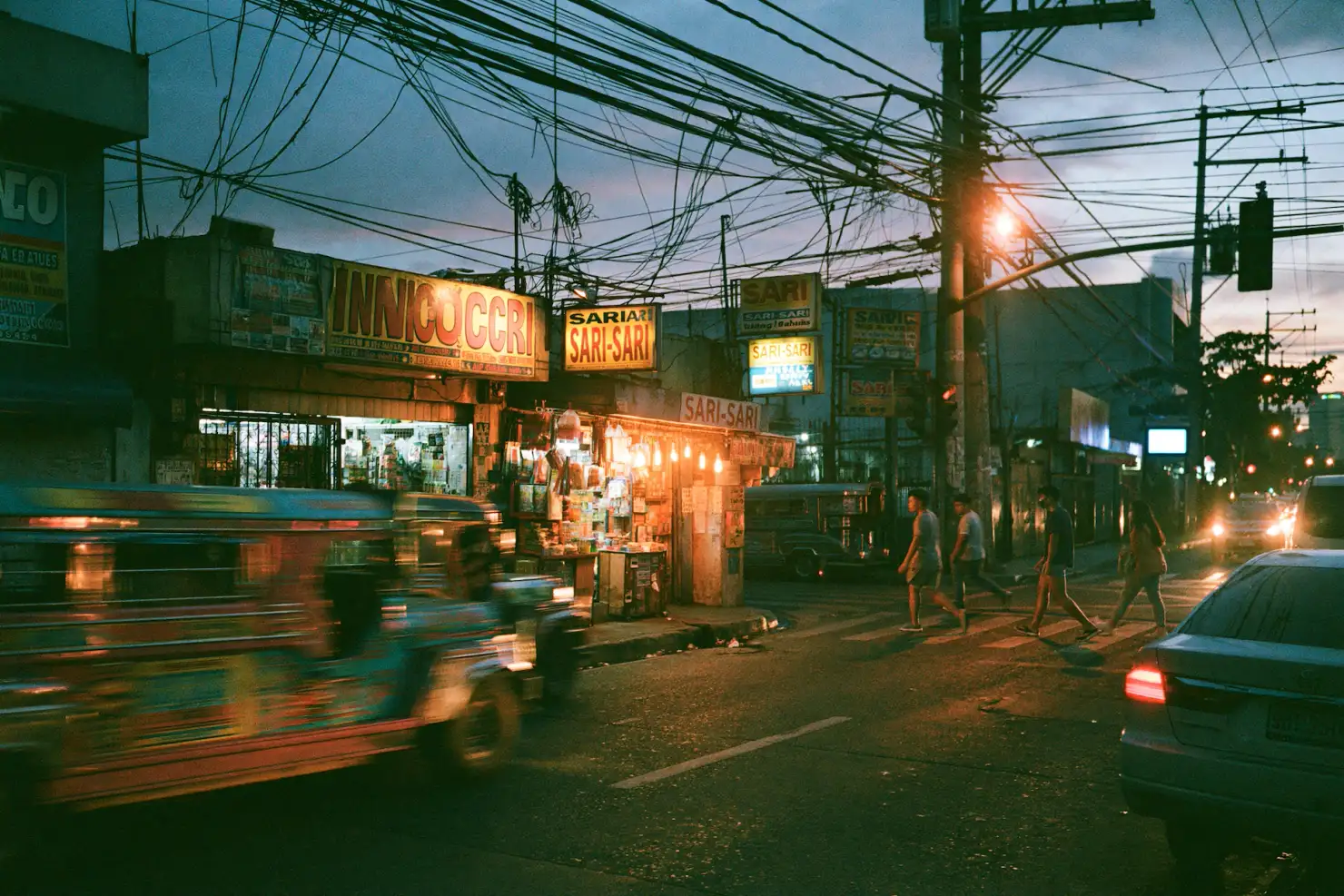 A Metro Manila street at dusk, glowing sari-sari store signs and tangled power lines, a jeepney blurring past as people cross