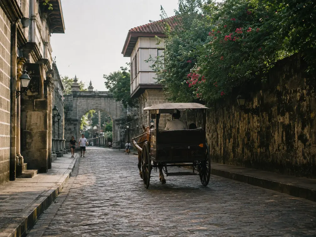A kalesa horse-carriage on a cobbled Intramuros street lined with old stone walls