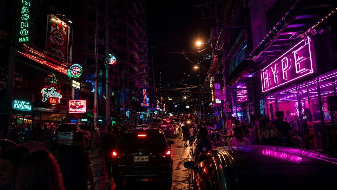 Neon bar signs lighting up a crowded Poblacion nightlife street in Manila after dark.