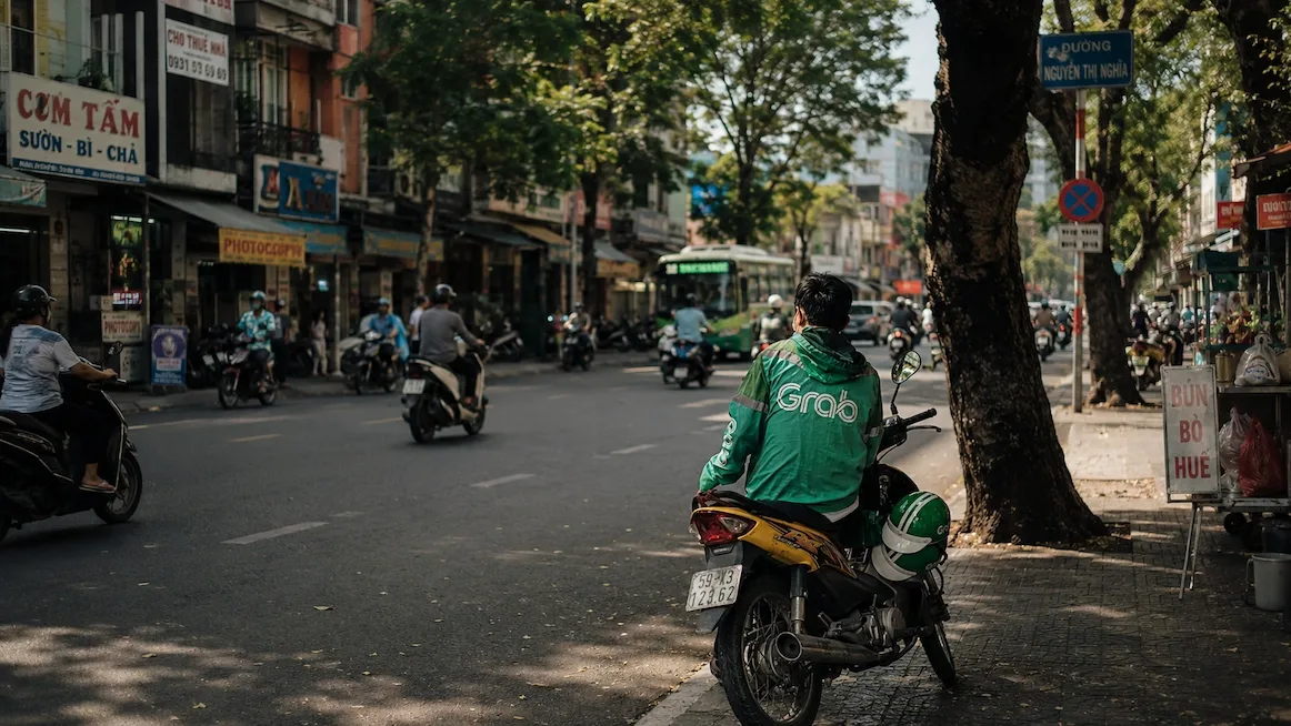 A Grab motorbike driver parked on a tree-lined Saigon street