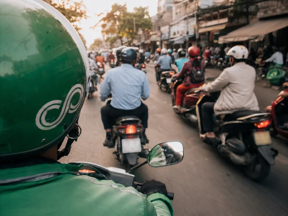 A pillion view over the shoulder of a green-jacketed Grab motorbike driver in Ho Chi Minh City traffic
