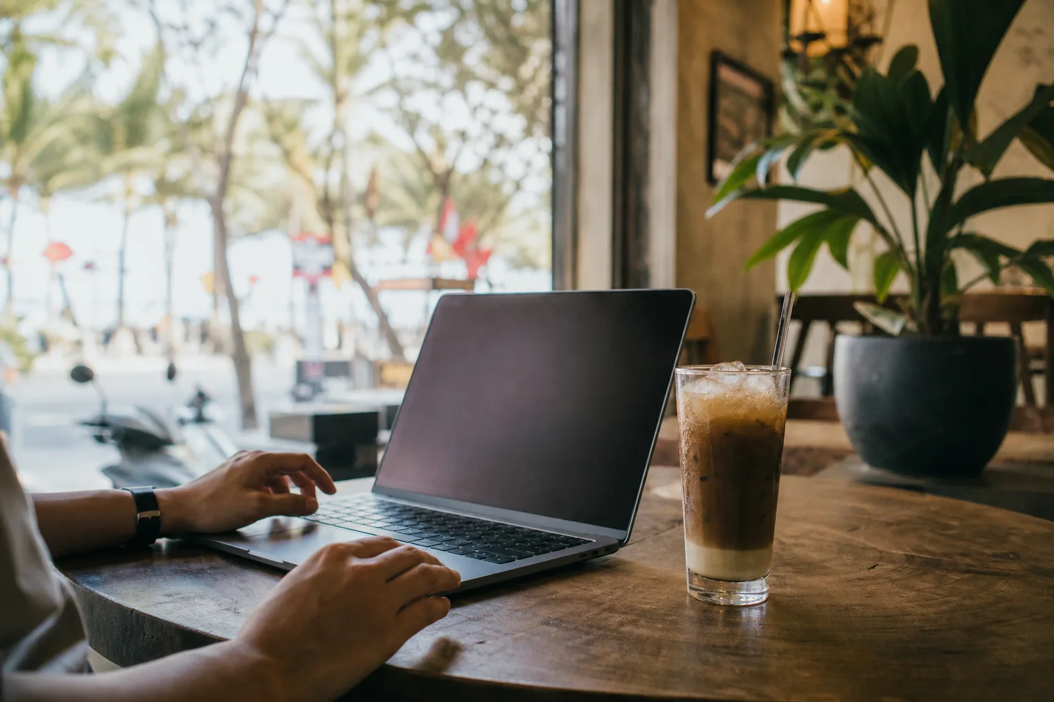 A laptop open on a cafe table in An Thuong, Da Nang, with a glass of iced Vietnamese coffee beside it