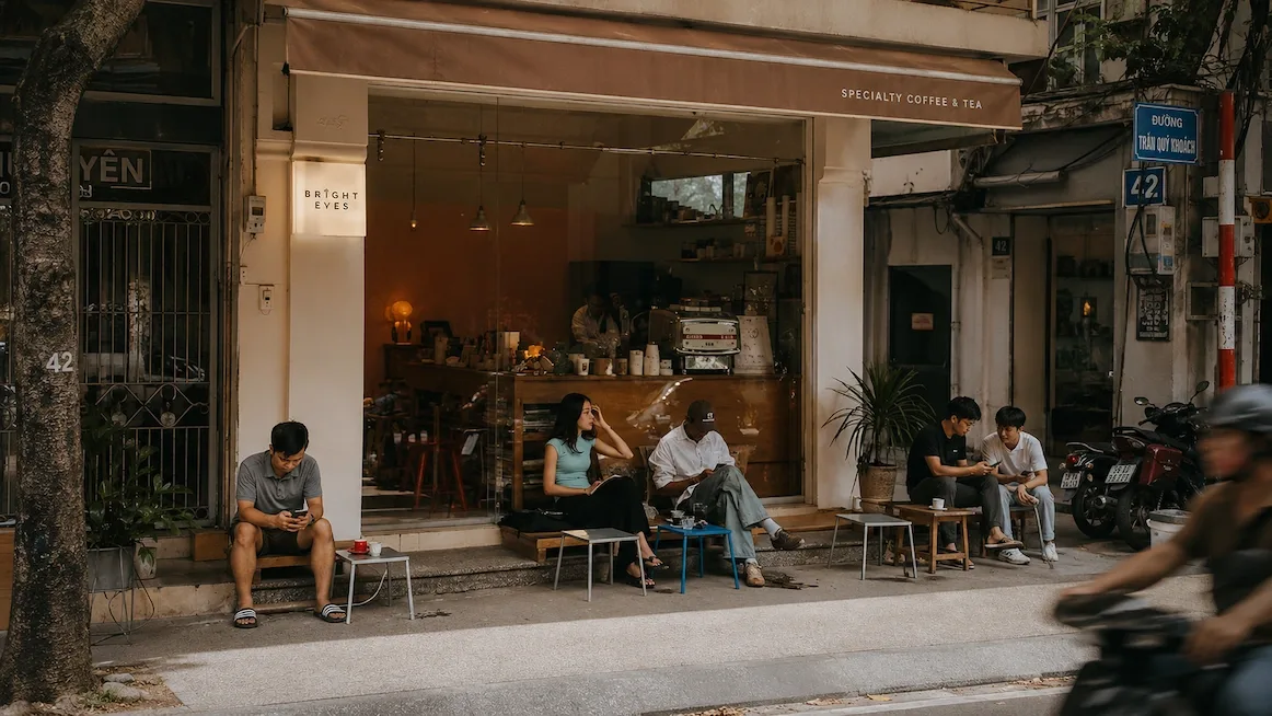 The open-air storefront of a specialty coffee shop on a Saigon street, with customers seated on low stools outside.