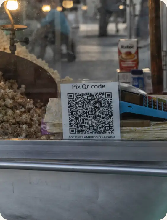 A handwritten Pix QR code sign taped inside a beachside popcorn stand’s glass case in Rio de Janeiro.