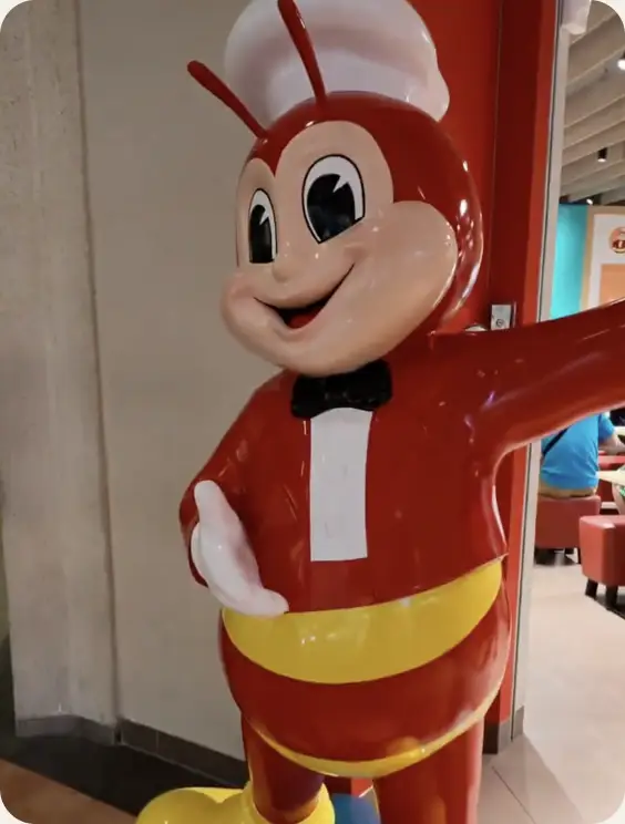 A red and yellow Jollibee mascot statue greeting customers inside a restaurant.