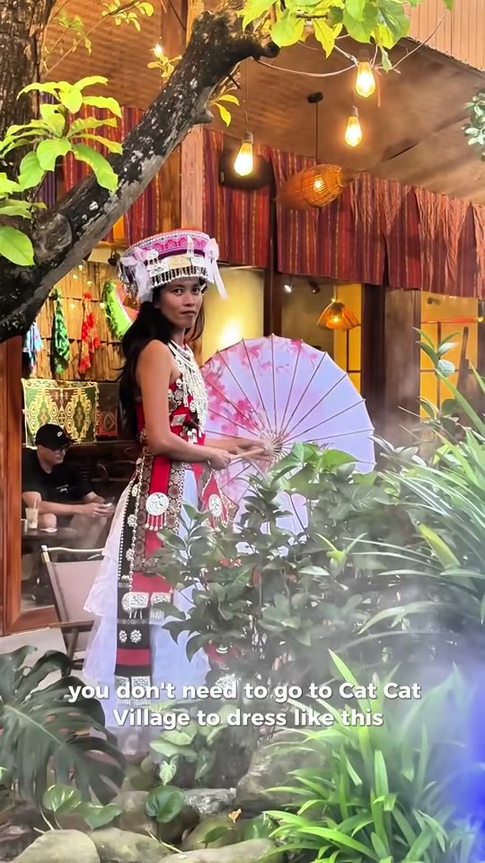 A traveler in a rented embroidered dress walks a garden path toward a costume-rental cafe in Da Nang.