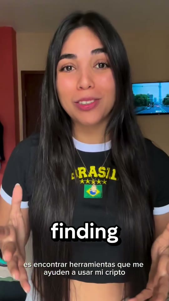 A young woman in a black Brasil ringer tee and a Brazil-flag pendant speaks to the camera in a São Paulo apartment.